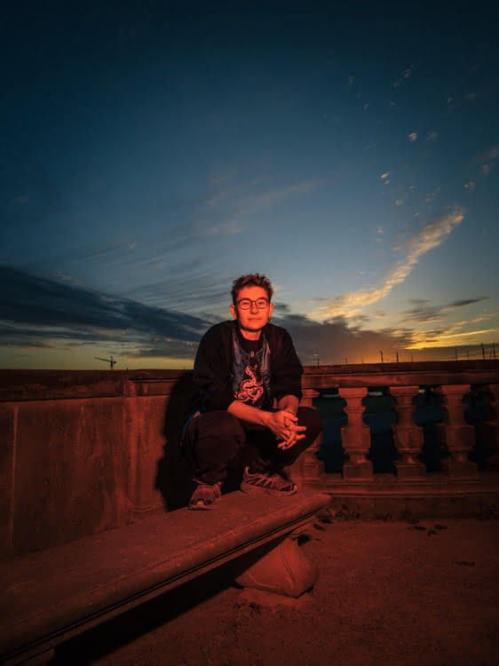 Person squatting on a stone bench at dusk.