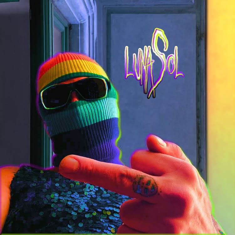 A person with a rainbow ski mask and glasses flashing a middle finger at the camera.