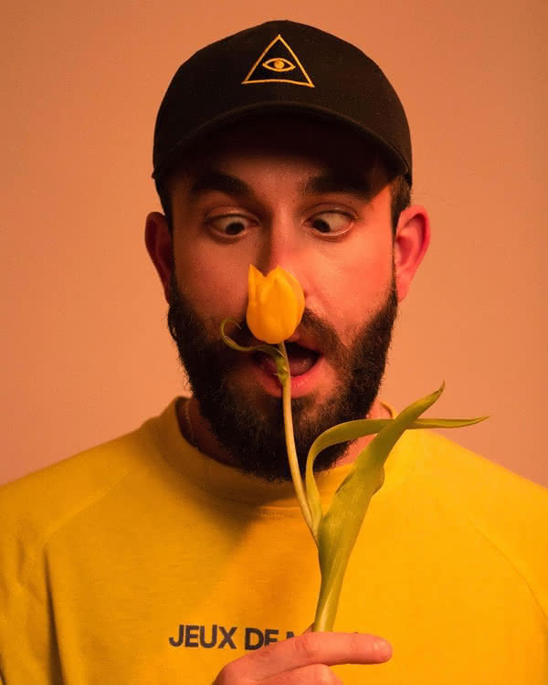 A person with a cap holding a yellow tulip close to their nose. Their eyes are focused on the flower blossom.